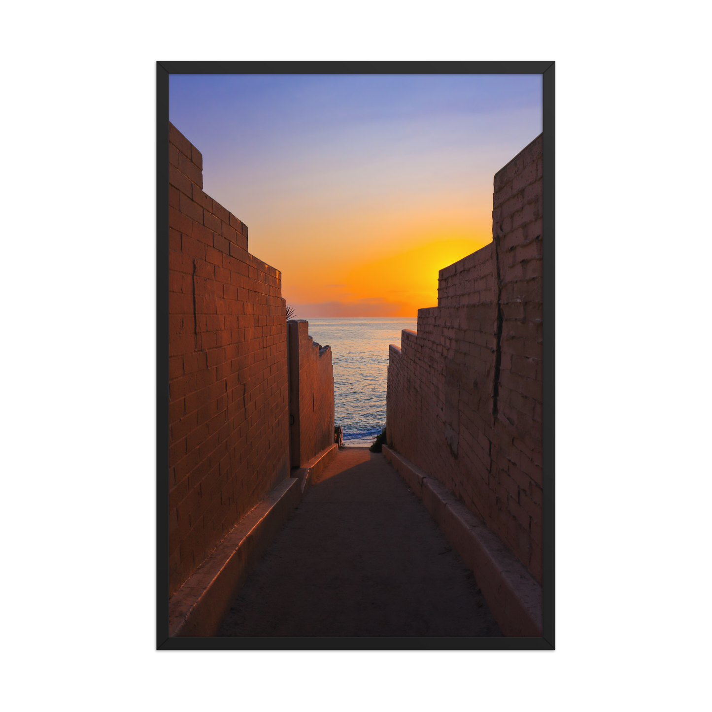 Pink coastal walls frame a narrow ocean view and a glowing sunset at the end of the passage in La Jolla; black frame, 24 × 36 inches.