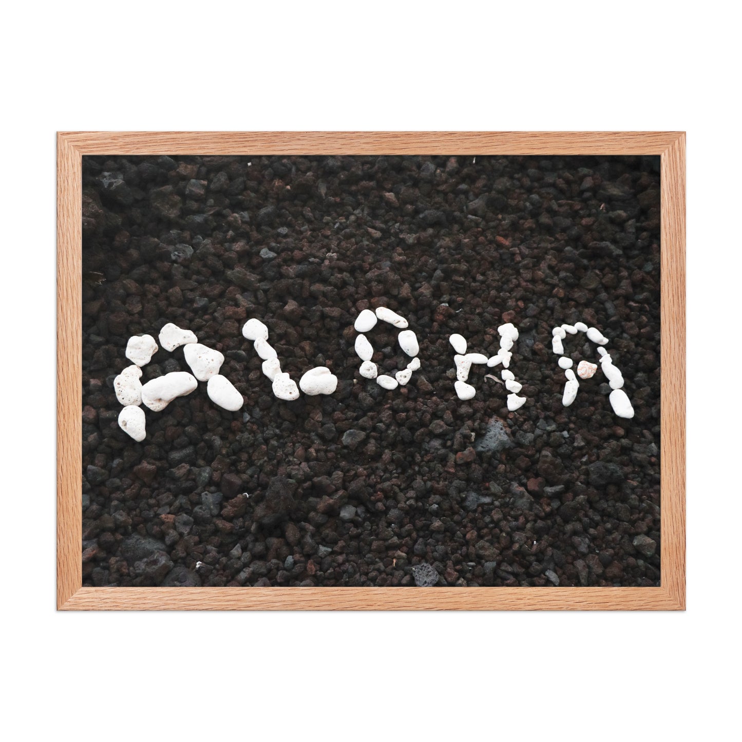 White stones spell Aloha against dark beach sand in a simple, graphic coastal composition; wood frame, 18 × 24 inches.