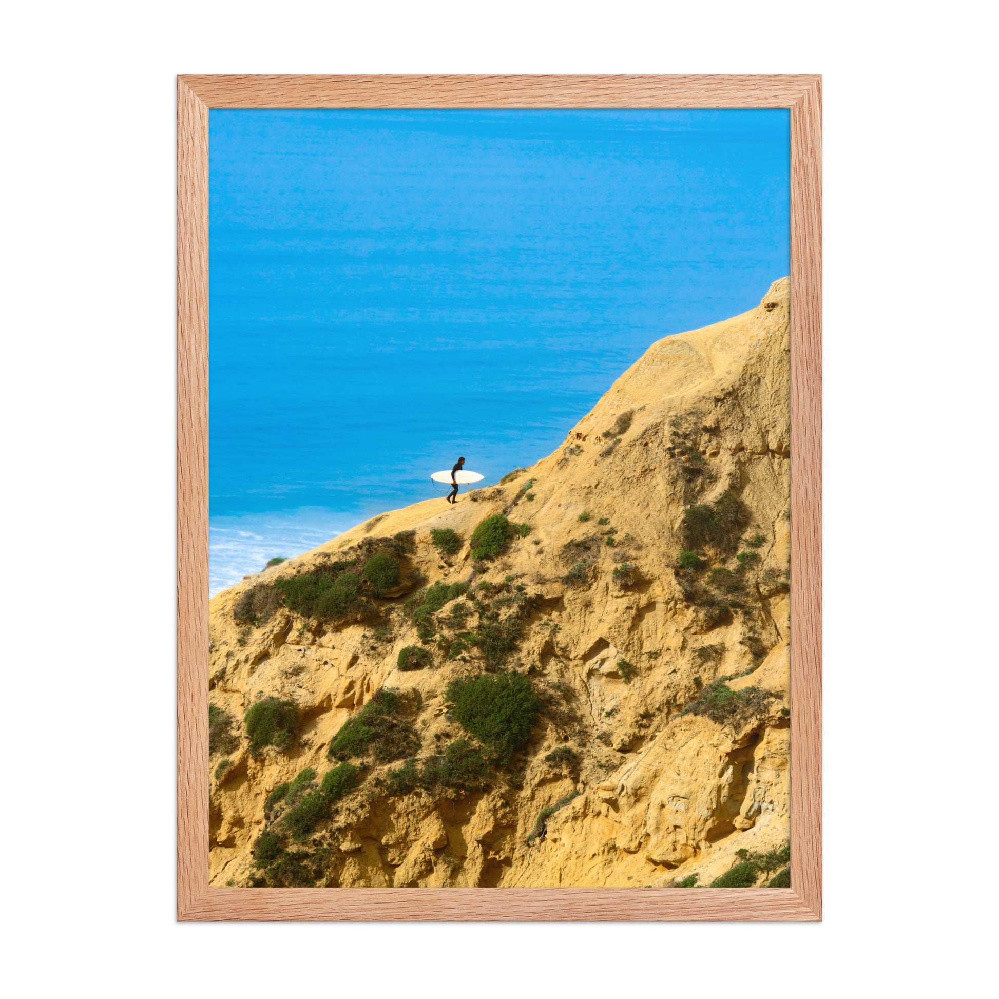 A narrow path winds along a sunlit coastal bluff above deep blue ocean water; wood frame, 18 × 24 inches.