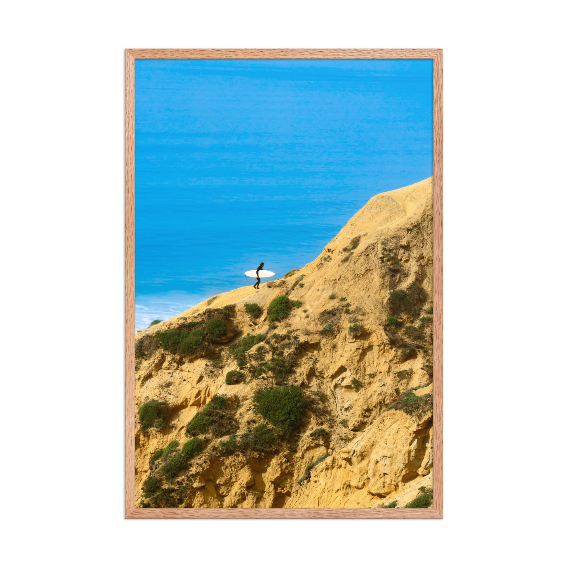A narrow path winds along a sunlit coastal bluff above deep blue ocean water; wood frame, 24 × 36 inches.