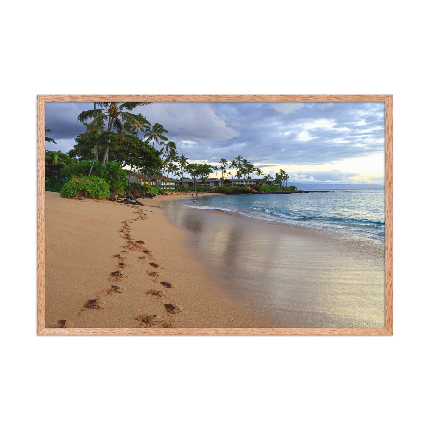 A trail of footprints crosses a quiet sandy beach beside gentle water and coastal vegetation; wood frame, 24 × 36 inches.