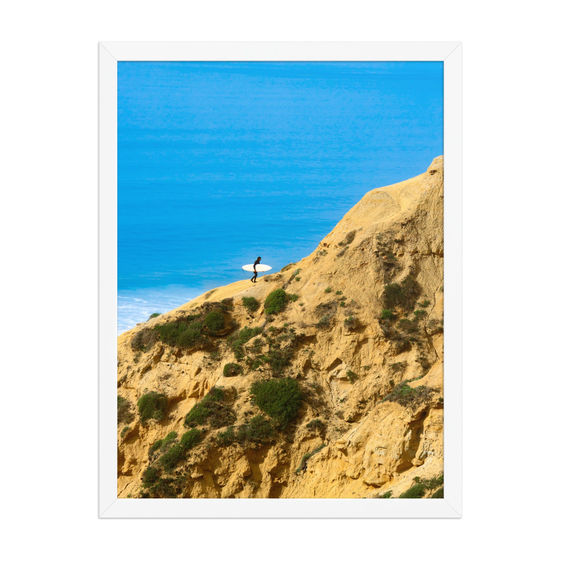 A narrow path winds along a sunlit coastal bluff above deep blue ocean water; white frame, 18 × 24 inches.