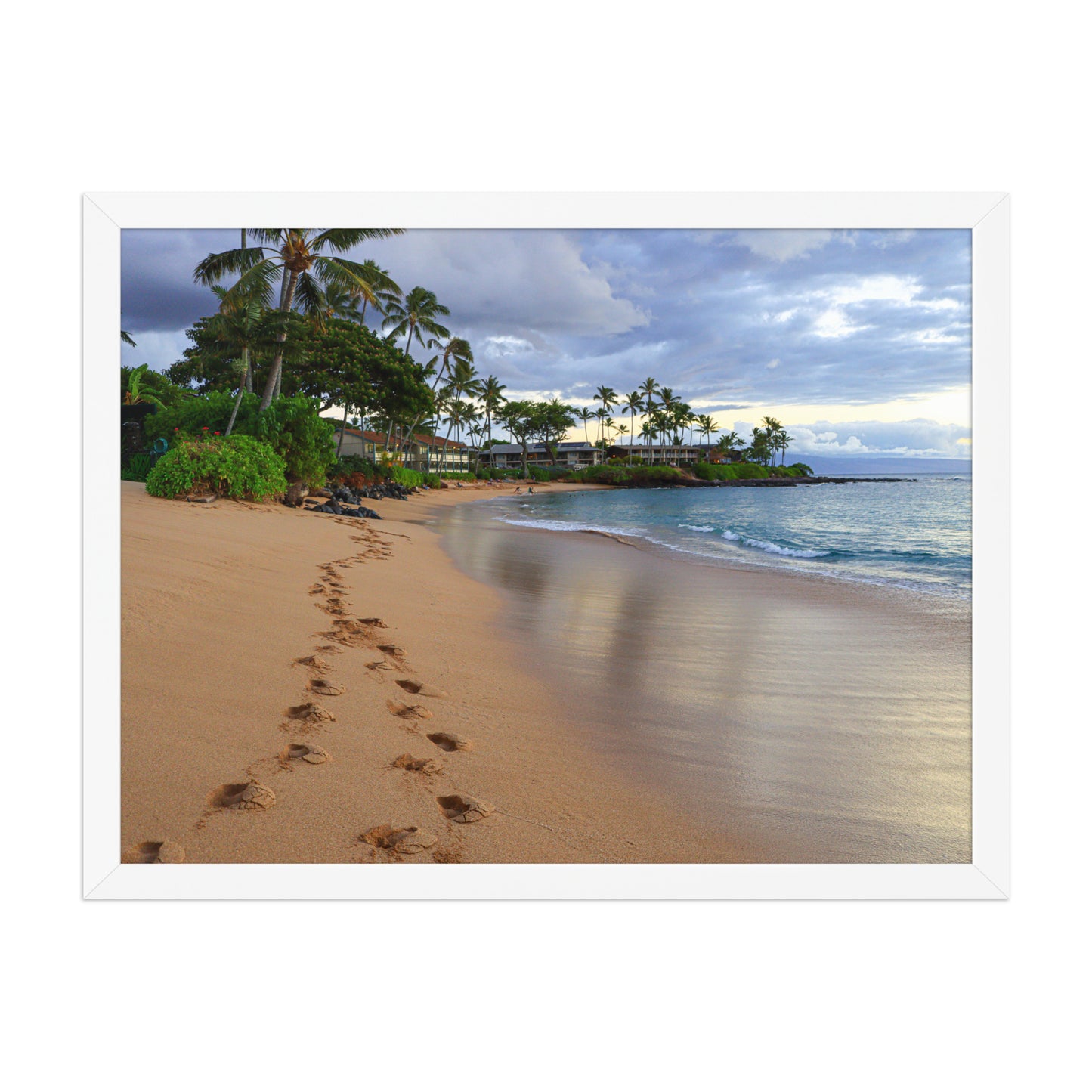 A trail of footprints crosses a quiet sandy beach beside gentle water and coastal vegetation; white frame, 18 × 24 inches.