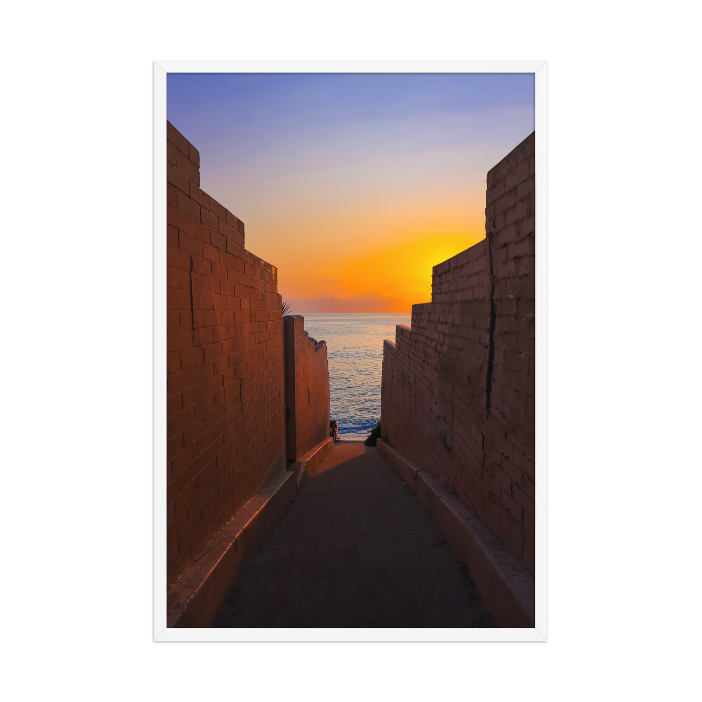 Pink coastal walls frame a narrow ocean view and a glowing sunset at the end of the passage in La Jolla; white frame, 24 × 36 inches.