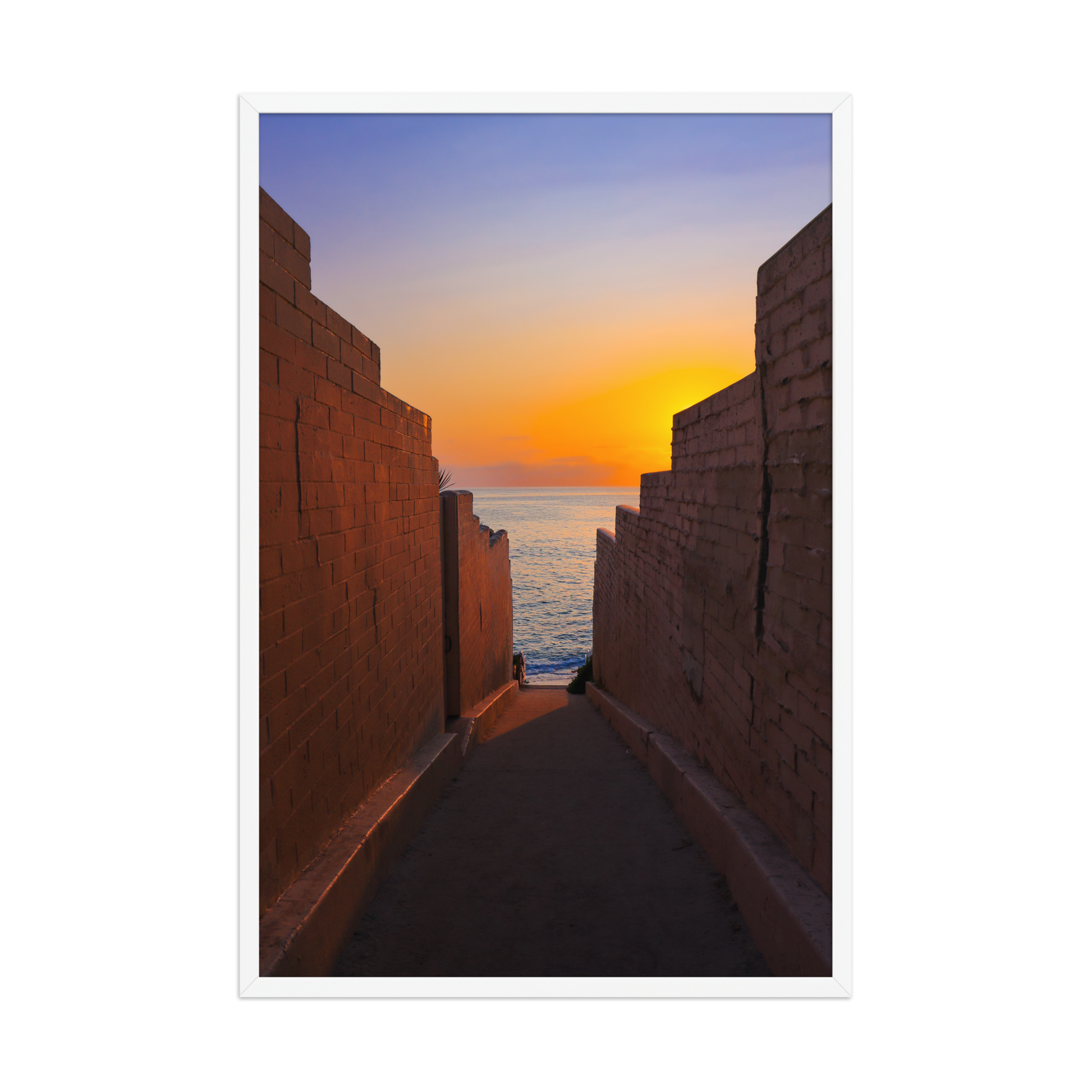 Pink coastal walls frame a narrow ocean view and a glowing sunset at the end of the passage in La Jolla; white frame, 24 × 36 inches.