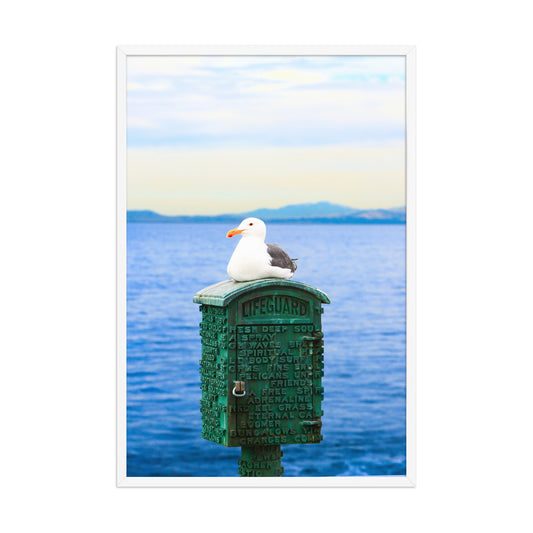 A seagull rests on a green coastal box above blue water, with a distant shoreline on the horizon; white frame, 24 × 36 inches.