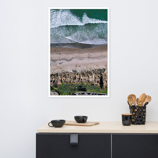 A group practices yoga above the beach as lines of white surf roll toward the shore; white frame, 24 × 36 inches.